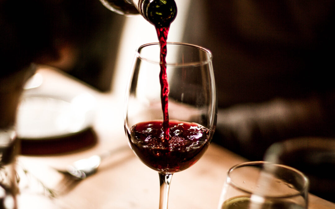 Red wine being poured into a stem glass at the table.